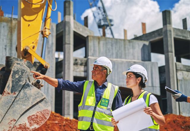 Engenheiros analisando o projeto em uma obra com escavadeira