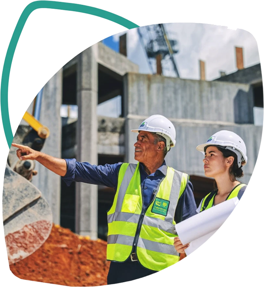 Engenheiros com capacete e colete analisando o projeto em uma obra com escavadeira