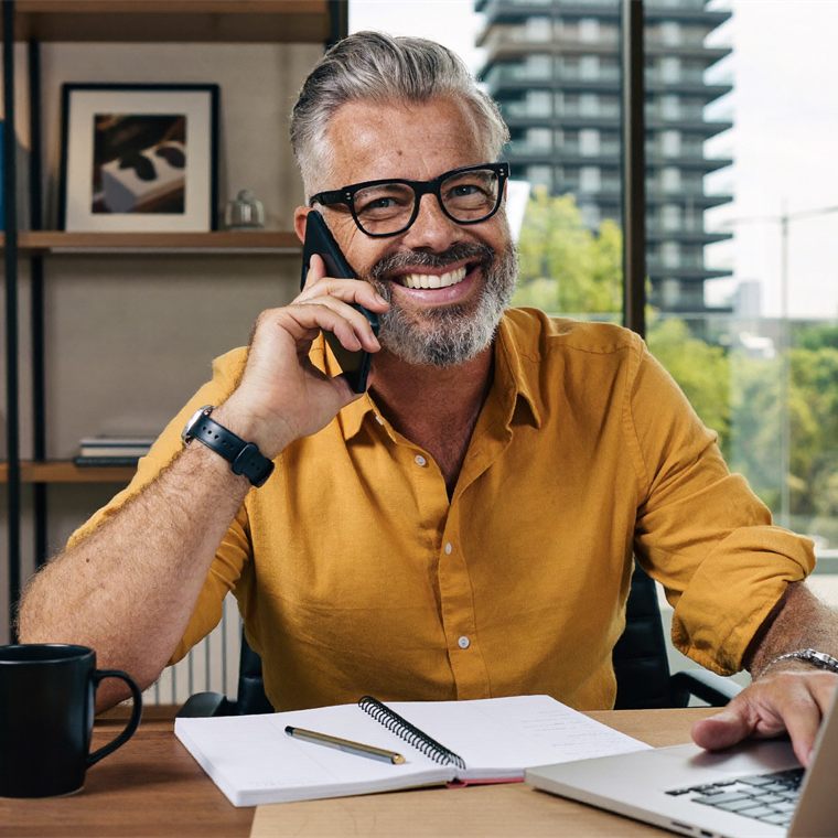 Investidor sorrindo ao telefone enquanto acompanha a aplicação no notebook