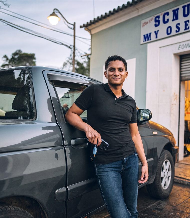 Lojista sorrindo em frente à sua revenda, ao lado de uma picape